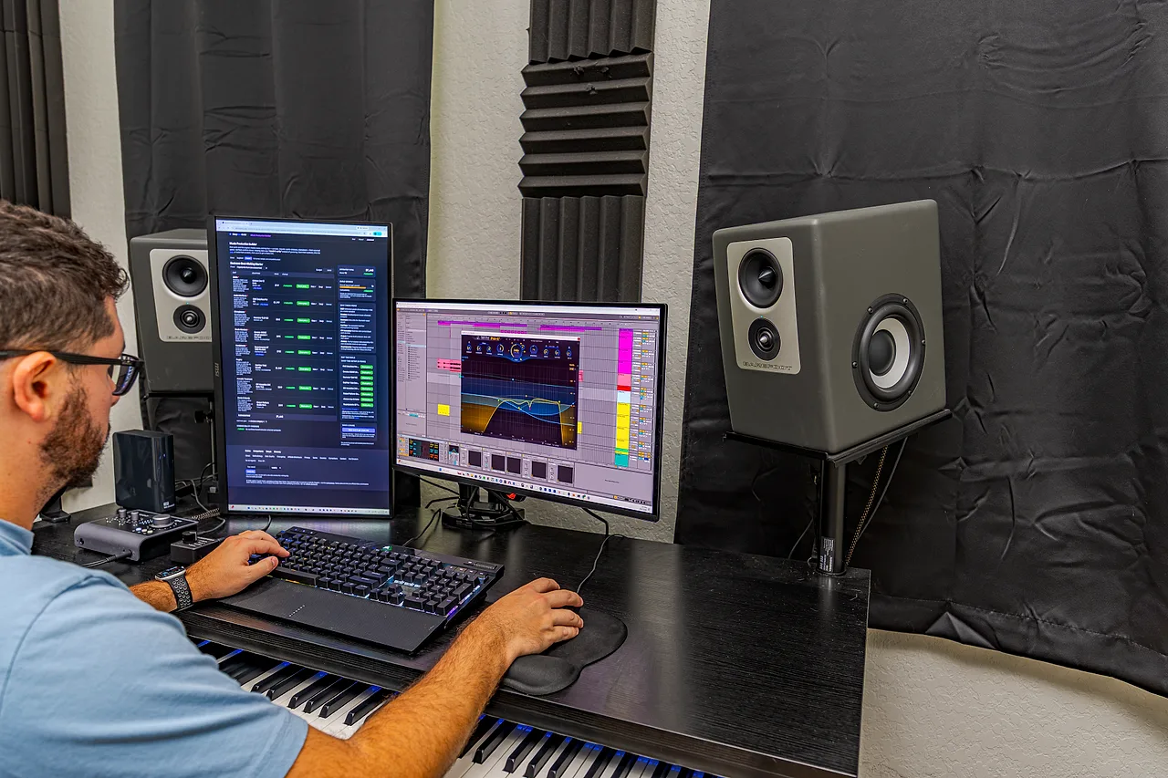 A person seated at a studio desk, one hand on the keyboard, an Ableton Live session open on screen